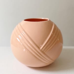 May include: A peach-colored ceramic vase with a round shape and a textured, geometric design. The vase has a smooth, glossy finish and a contrasting orange interior. The decorative vase is suitable for displaying flowers or as a standalone art piece.