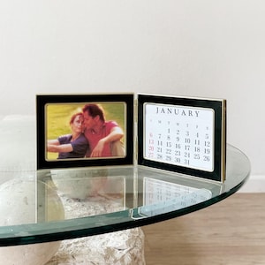 May include: A black and gold picture frame with a photo of a couple in the left side and a calendar for January on the right side. The calendar shows the month of January with the dates 1 through 31.