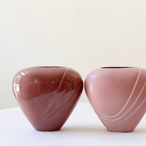 May include: Two heart-shaped ceramic vases, one in a deep burgundy red and the other in a light pink. Both vases have a swirl design.