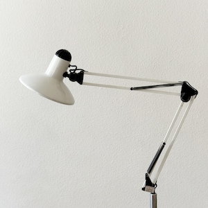 May include: A white and black adjustable desk lamp with a rounded lampshade. The lamp has a silver-colored base and arm, with black joints and a black top on the lampshade. The lamp is designed to be adjustable.