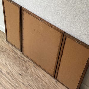 May include: Three wooden picture frames with brown cardboard backing. The frames are arranged in a row, with the largest frame in the middle and the two smaller frames on either side.