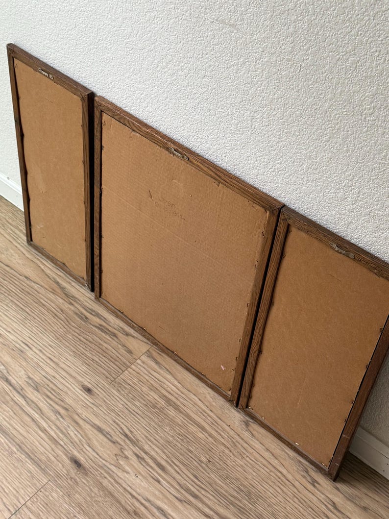 May include: Three wooden picture frames with brown cardboard backing. The frames are arranged in a row, with the largest frame in the middle and the two smaller frames on either side.