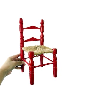 May include: A small red wooden chair with a woven straw seat. The chair has a simple design with four legs and a back.