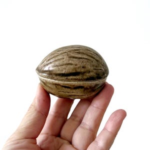 Puede incluir: Una caja de cerámica para baratijas con forma de nuez, con un esmalte moteado marrón y gris.