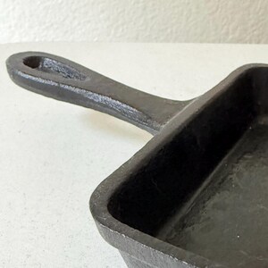Puede incluir: Una sart&eacute;n de hierro fundido negro con una superficie de cocci&oacute;n rectangular y un asa. El asa tiene un agujero para colgar. La sart&eacute;n est&aacute; hecha de metal resistente y est&aacute; dise&ntilde;ada para cocinar.