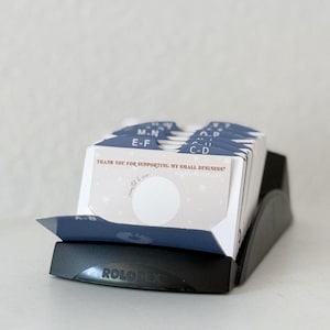 May include: A black Rolodex card file with navy blue and white dividers labeled A-B, C-D, E-F, and M-N. The cards have a star pattern and the text "THANK YOU FOR SUPPORTING MY SMALL BUSINESS!" is visible.