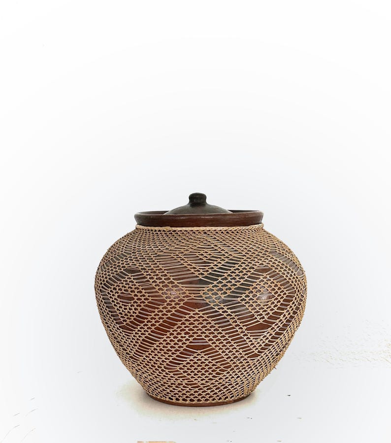 Op de afbeelding: Een bruine keramische pot met een geweven, lichtbruin roosterontwerp. De pot heeft een donkerbruine rand en een bijpassende deksel. De pot is rond met een licht bolvormige vorm. De achtergrond is wit.