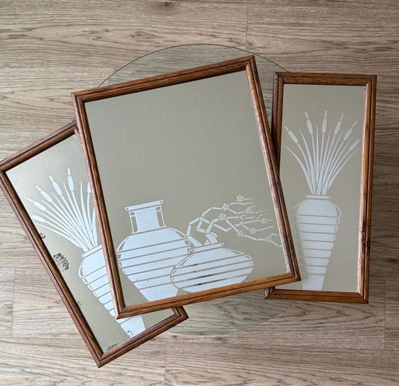 May include: Three framed mirrors with a beige background and white stylized illustrations of vases and reeds. The mirrors are in wooden frames with a dark brown finish.