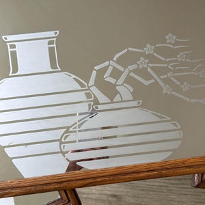 May include: A mirrored tray with a wooden frame features an etched design of two vases and a flowering branch. The vases are striped and the branch has delicate flowers.