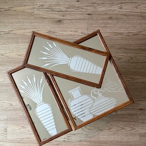 May include: Three framed wall mirrors with a white silhouette design of stylized plants and vases. The mirrors have a brown wooden frame.
