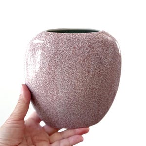 May include: A speckled pink ceramic vase with a rounded oval shape.