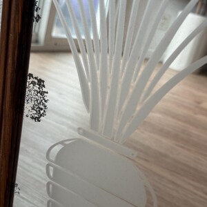 May include: A white etched design of a plant with long leaves and a round bulbous base on a frosted glass surface.