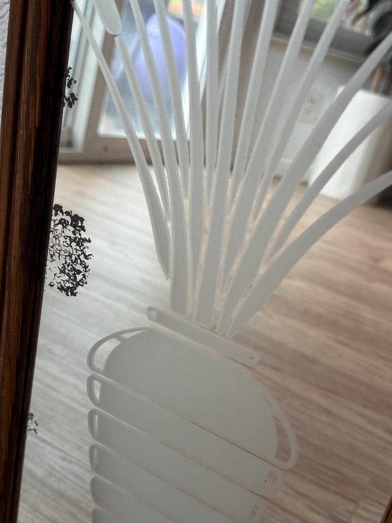 May include: A white etched design of a plant with long leaves and a round bulbous base on a frosted glass surface.
