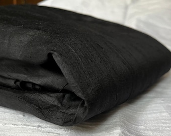 Könnte beinhalten: Ein schwarzer Seidenstoff, der in zwei Hälften gefaltet ist und die Textur des Stoffes zeigt.