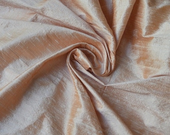 May include: A close-up of a peach-colored silk fabric with a subtle shimmer. The fabric is draped and folded, creating soft, flowing lines.