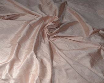 May include: A close-up of a smooth, pale pink fabric with a soft, flowing texture. The fabric is draped and folded, creating a sense of movement and elegance.