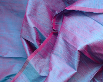 May include: Close-up of a blue and pink silk fabric with a subtle shimmer. The fabric is folded and draped, showcasing its texture and drape.