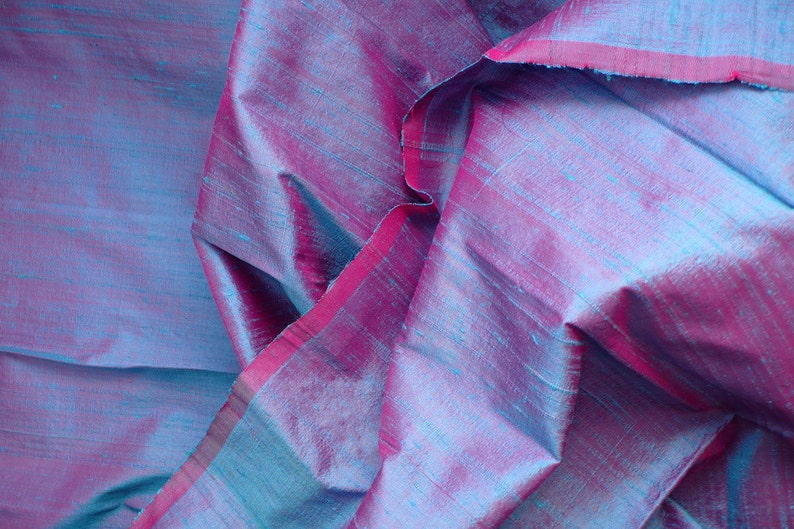 Peut inclure: Gros plan sur un tissu de soie bleu et rose avec un l&eacute;ger chatoiement. Le tissu est pli&eacute; et drap&eacute;, mettant en valeur sa texture et son drap&eacute;.