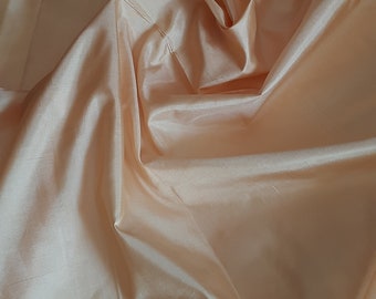 May include: A close-up of a smooth, peach-colored fabric with soft folds and wrinkles.