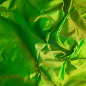 Puede incluir: Primer plano de una tela verde brillante con una textura suave y sedosa. La tela está doblada y drapeada, creando líneas suaves y fluidas.