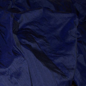 Puede incluir: Primer plano de una tela azul oscuro con una textura suave y sedosa. La tela est&aacute; doblada y drapeada, creando l&iacute;neas suaves y fluidas.