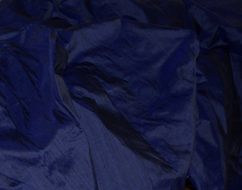 Puede incluir: Primer plano de una tela azul oscuro con una textura suave y sedosa. La tela est&aacute; doblada y drapeada, creando l&iacute;neas suaves y fluidas.