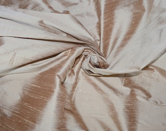 May include: A length of light beige or champagne-colored fabric with a distinct slubbed texture. The material features a subtle sheen and is gathered in the center, creating deep, flowing folds and shadows that highlight the fabric's surface.