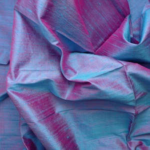 Peut inclure: Gros plan sur un tissu iridescent bleu et violet &agrave; la texture soyeuse. Le tissu est pli&eacute; et drap&eacute;, r&eacute;v&eacute;lant l'effet chatoyant des couleurs.