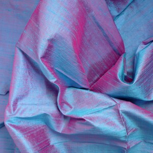 Peut inclure: Gros plan sur un tissu iridescent bleu et rose avec une texture soyeuse. Le tissu est pli&eacute; et drap&eacute;, cr&eacute;ant un aspect doux et fluide.