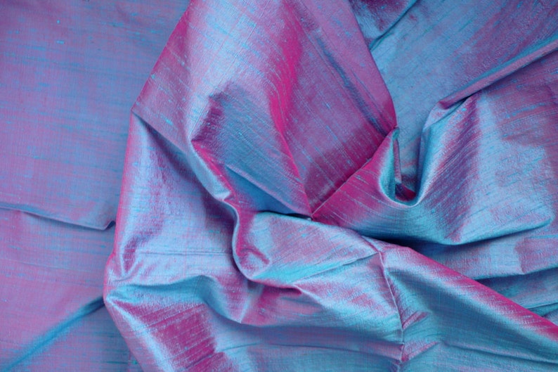 Peut inclure: Gros plan sur un tissu iridescent bleu et rose avec une texture soyeuse. Le tissu est pli&eacute; et drap&eacute;, cr&eacute;ant un aspect doux et fluide.