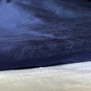Puede incluir: Primer plano de una tela azul oscuro con un sutil patr&oacute;n texturizado. La tela est&aacute; doblada sobre una tela blanca.
