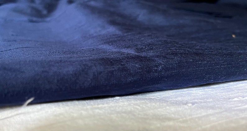 Puede incluir: Primer plano de una tela azul oscuro con un sutil patr&oacute;n texturizado. La tela est&aacute; doblada sobre una tela blanca.