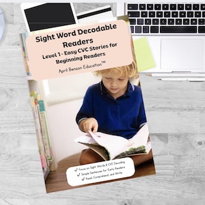 May include: A book titled "Sight Word Decodable Readers" with a child reading. The cover is light peach with black text. The book is open, revealing pages with illustrations. The text on the cover reads "Level 1 - Easy CVC Stories for Beginning Readers".