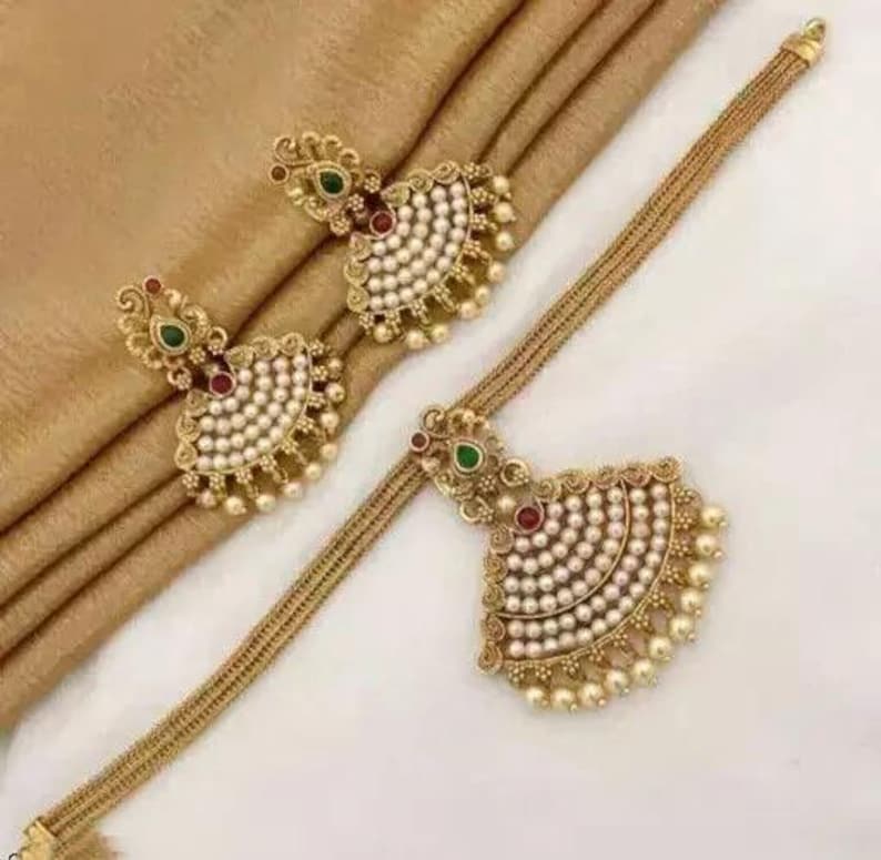 May include: A gold-toned jewelry set featuring a necklace and matching earrings. The set includes a necklace with a fan-shaped pendant and earrings with a similar design. Each piece is adorned with small pearls and red and green accents.
