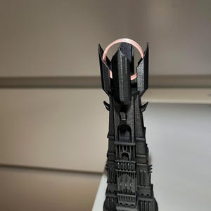May include: A black, 3D-printed model of a tall tower with intricate architectural details. The tower has a circular base and a pink ring at the top. The model is likely a replica of a fantasy structure.