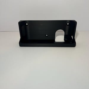 May include: A black plastic license plate holder with a rectangular shape. It has a curved base and a series of holes for mounting. The holder features a cutout for the license plate light.