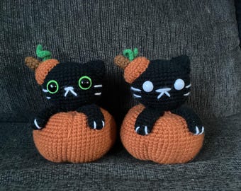 May include: Two handmade crochet black cat figurines, each perched inside an orange pumpkin. The cats have green eyes, white whiskers, and are wearing pumpkin hats. A charming Halloween or fall-themed decoration.