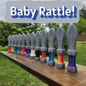 May include: A row of gray baby rattles with colorful bases, including red, yellow, green, pink, purple, white, black, orange, rainbow, and blue. The text "Baby Rattle!" is displayed above the rattles.