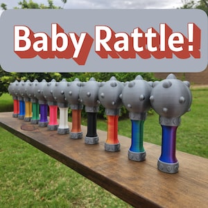 May include: A row of gray baby rattles with colorful handles. Each rattle has a spherical head with small bumps. The handles are various colors, including red, blue, green, and rainbow gradients. The text "Baby Rattle!" is displayed above.
