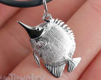 May include: Silver pendant necklace featuring a detailed, three-dimensional fish design. The fish has a long, pointed snout and a textured, scaly body.