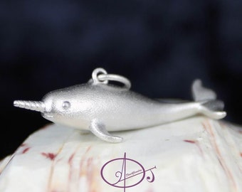 May include: A silver narwhal charm pendant, a popular choice for jewelry making. The charm is detailed with a small, curled tusk and a smooth, rounded body.