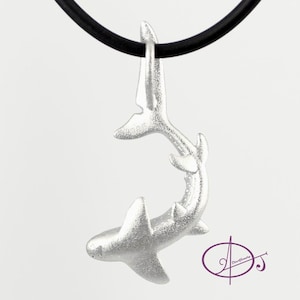 May include: A silver shark pendant necklace on a black cord. The shark is in a curled position with its tail up and its head down. The pendant is detailed and realistic.