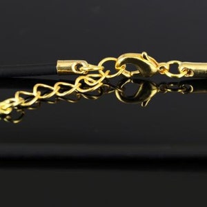 K&ouml;nnte beinhalten: Nahaufnahme einer schwarzen Schnurkette mit einem goldenen Verschluss und einer Verl&auml;ngerungskette. Die Kette liegt auf einer schwarzen Oberfl&auml;che.
