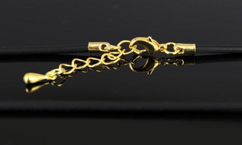 K&ouml;nnte beinhalten: Nahaufnahme einer schwarzen Schnurkette mit einem goldenen Verschluss und einer Verl&auml;ngerungskette. Die Kette liegt auf einer schwarzen Oberfl&auml;che.