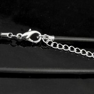 May include: A close-up of a black cord necklace with a silver clasp and chain extender. The necklace is on a black surface.