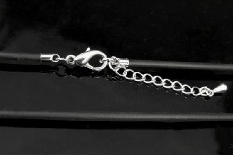 May include: A close-up of a black cord necklace with a silver clasp and chain extender. The necklace is on a black surface.