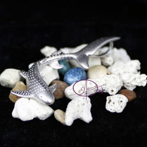 May include: Two silver whale shark figurines on a bed of white coral and blue stones. The sharks are detailed with spots and fins.