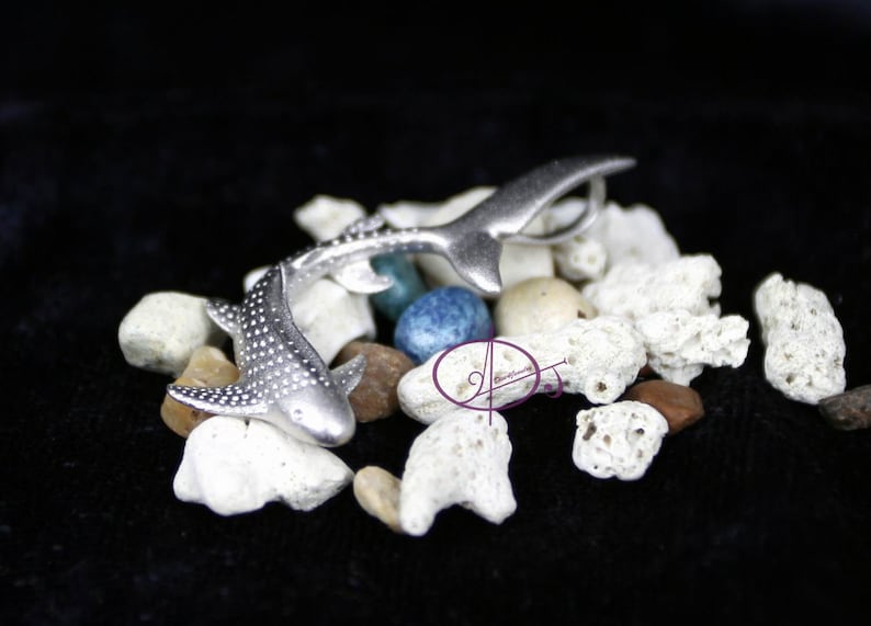 May include: Two silver whale shark figurines on a bed of white coral and blue stones. The sharks are detailed with spots and fins.