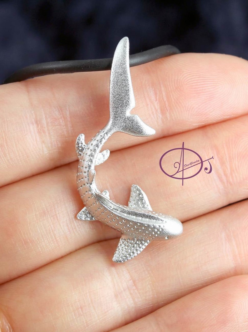 May include: Silver whale shark pendant necklace. The shark is detailed with a spotted pattern and has a curved tail fin.
