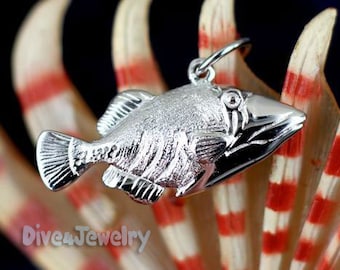 May include: A silver fish pendant charm with a detailed, textured design. The pendant is shaped like a triggerfish and has a loop at the top for attaching to a chain or bracelet.